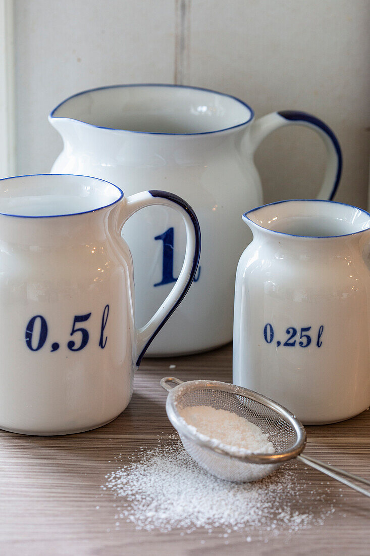 Porcelain measuring cups in various sizes and a sieve with icing sugar