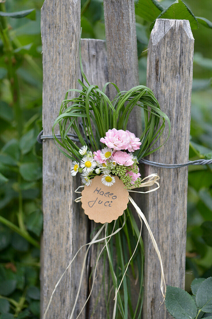 Heart of grasses with roses and daisies with pendant on garden fence