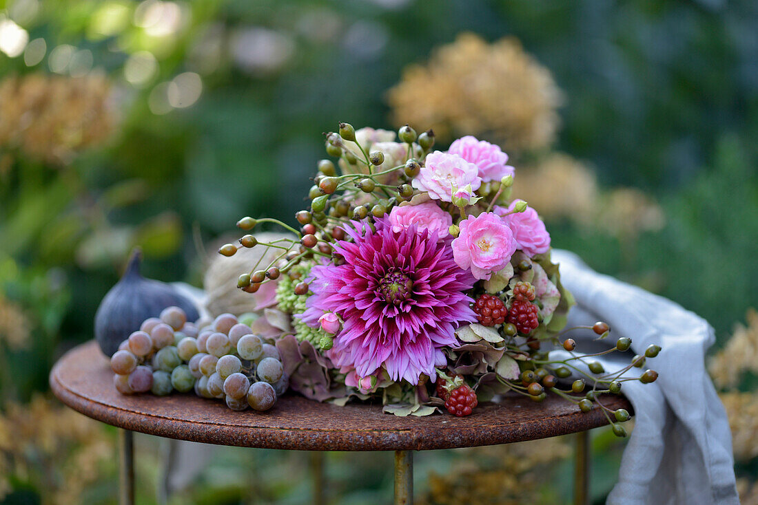 Late summer bouquet of hydrangeas, dahlias, roses, rose hips and blackberries on a metal table decorated with grapes and figs