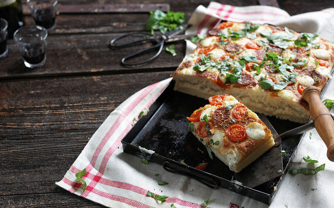 Blechpizza mit Tomaten, Salami, Mozzarella und Basilikum