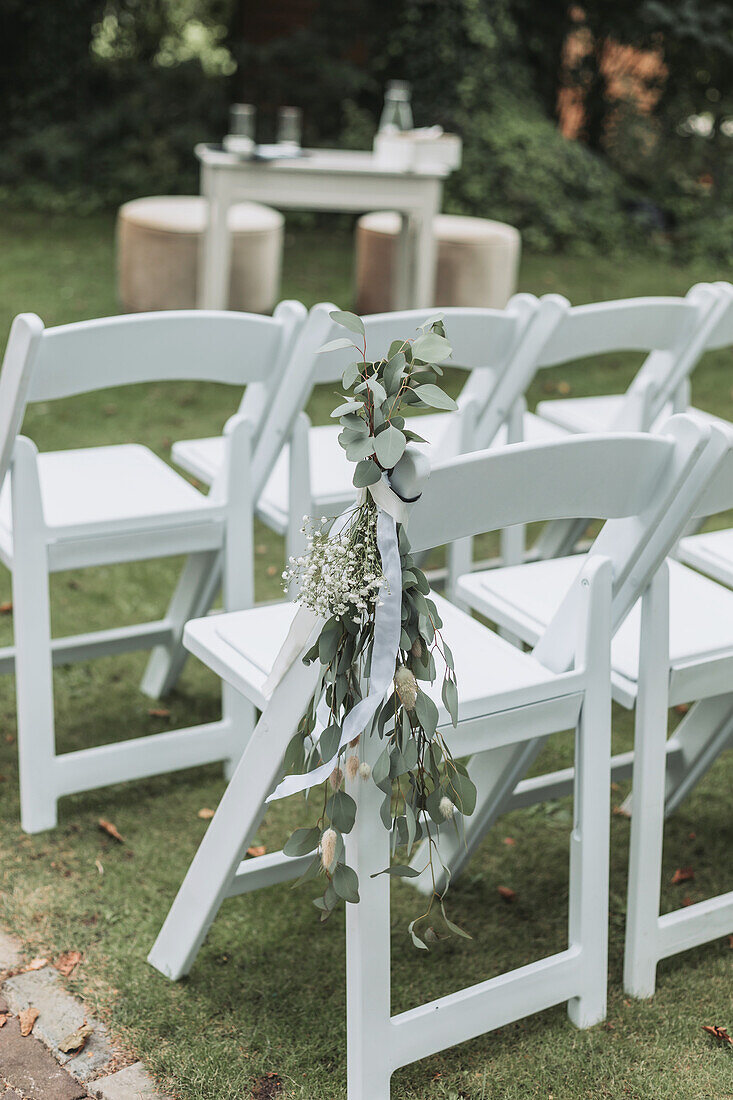 White garden chairs decorated with eucalyptus branches