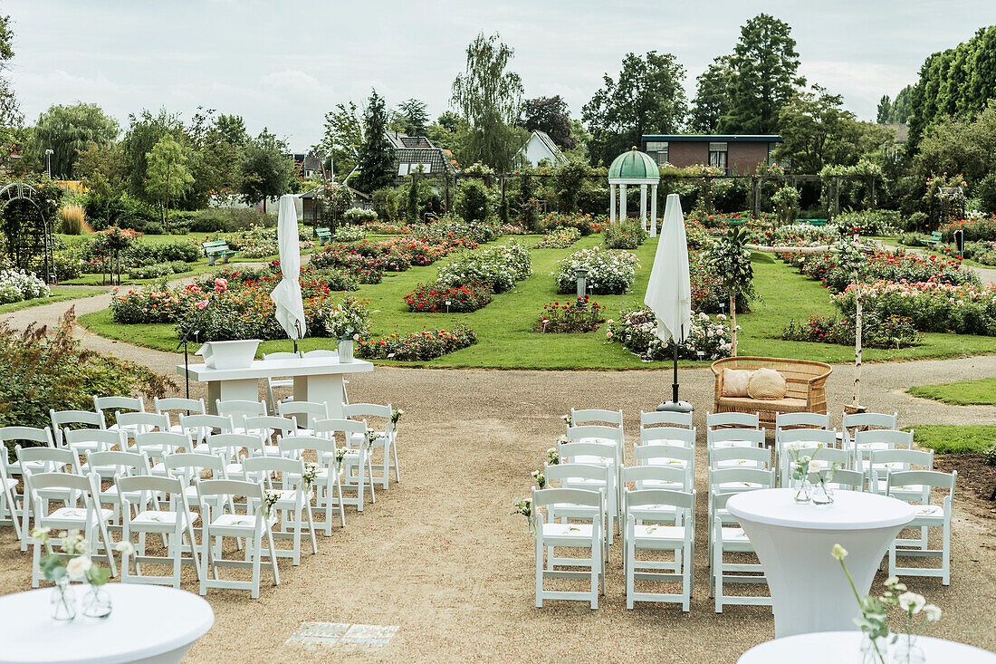 Outdoor wedding ceremony in rose garden with white seating