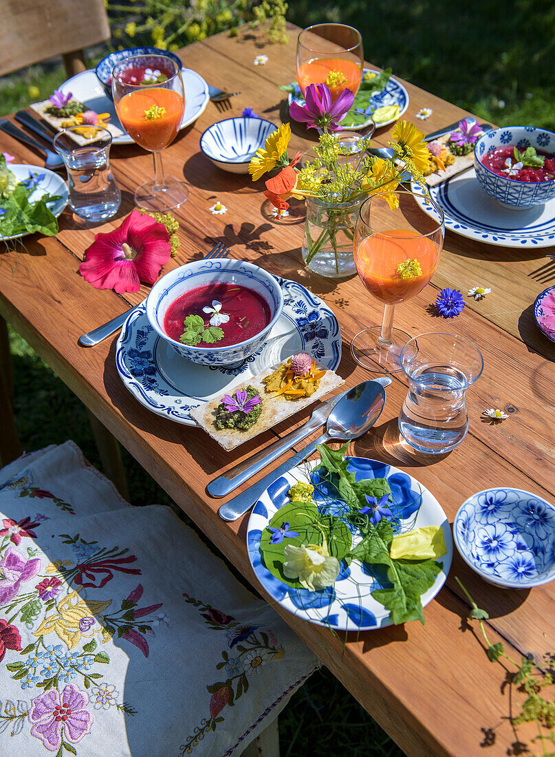 Gedeckter Holztisch im sommerlichen Garten mit Getränken und Essen