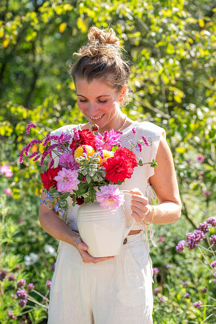 Frau trägt Vase mit buntem Strauß aus Dahlien (Dahlia), orientalischen Knöteriche (Persicaria orientalis), Bartblume (Caryopteris), und Borretsch