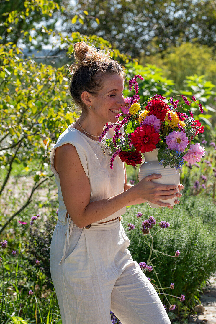 Frau riecht an buntem Strauß mit Dahlien (Dahlia), orientalischen Knöteriche (Persicaria orientalis), Bartblume (Caryopteris), und Borretsch