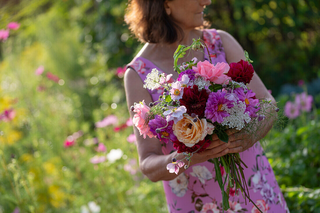 Frau mit Blumenstrauß aus Dahlien (Dahlia), Rosen (Rosa), Herbstanemonen (Anemone Hupehensis) und wilde Möhre