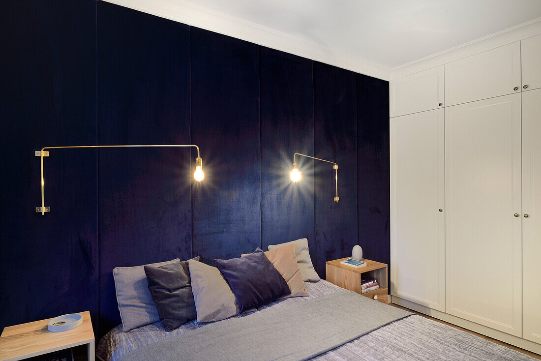 Bedroom with dark blue wall paneling, built-in wardrobes and modern wall lamps