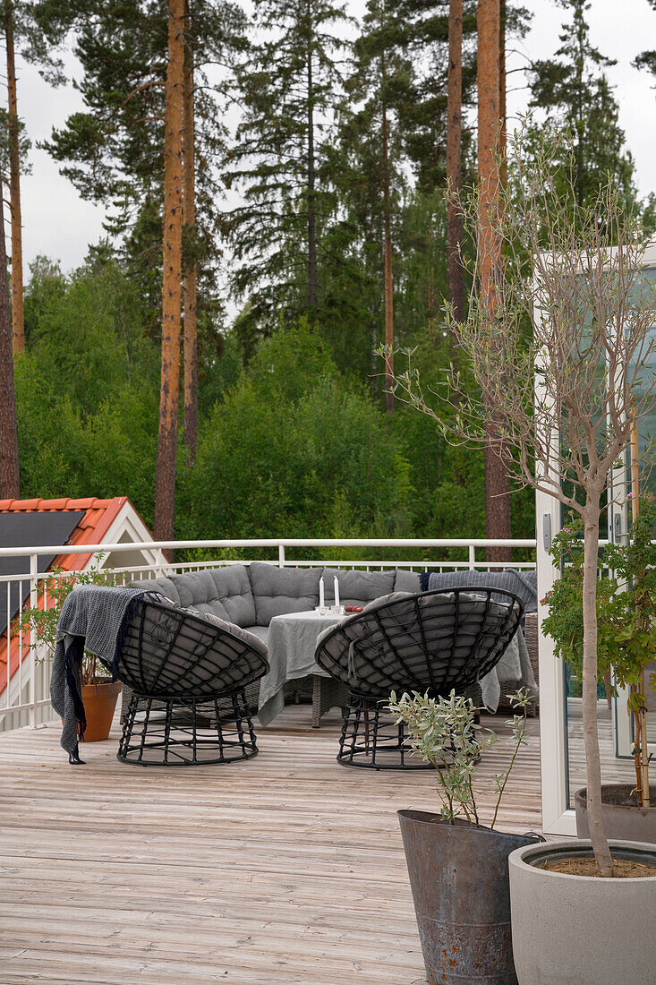 Sitzbereich auf Holzterrasse mit schwarzen Korbstühlen und großem Sofa