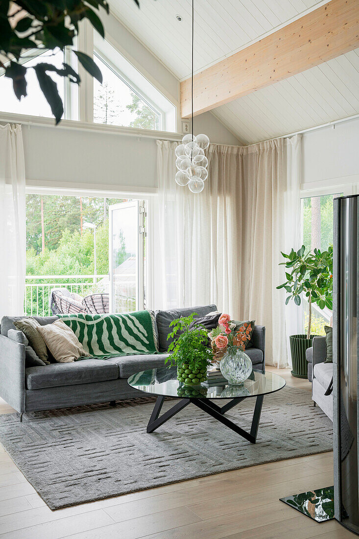 Bright living room with grey sofa, glass table and indoor plants