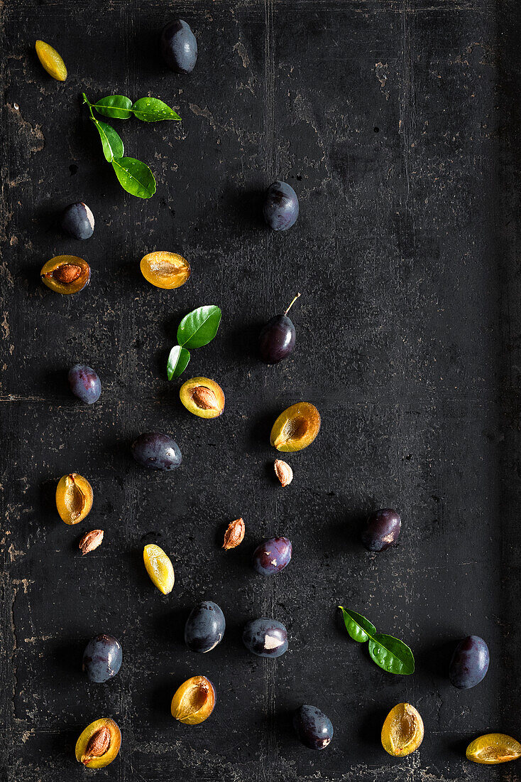 Whole and halved plums with pips on a dark background