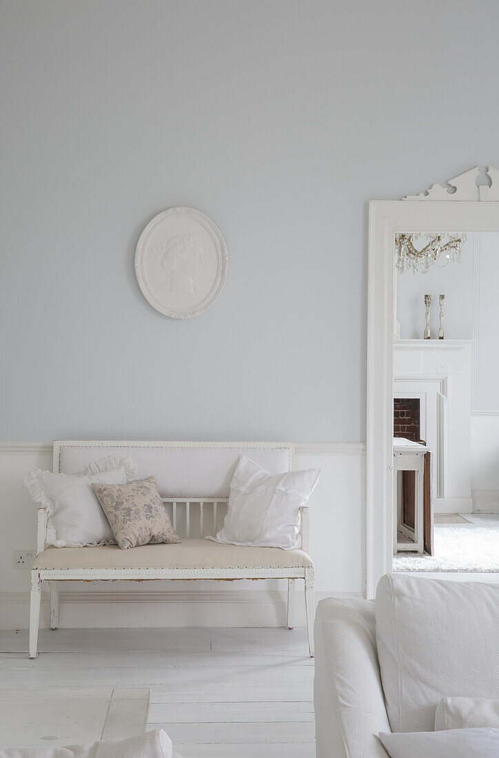 White living room with antique bench and cushions, view into the neighbouring room