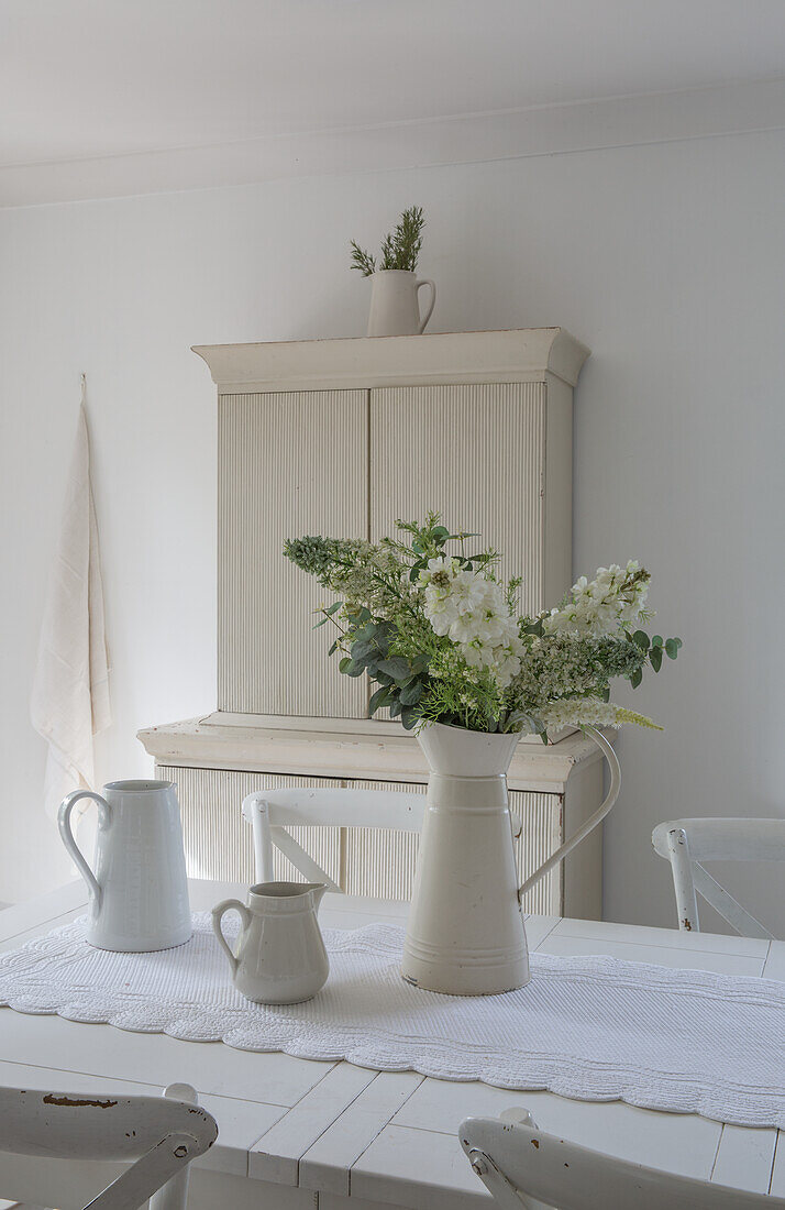 Weißes Landhaus-Esszimmer mit Tischdeko aus Milchkrügen und Blumenstrauß