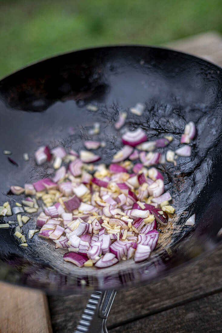 Rote Zwiebeln mit Knoblauch und Gewürzen im Wok andünsten