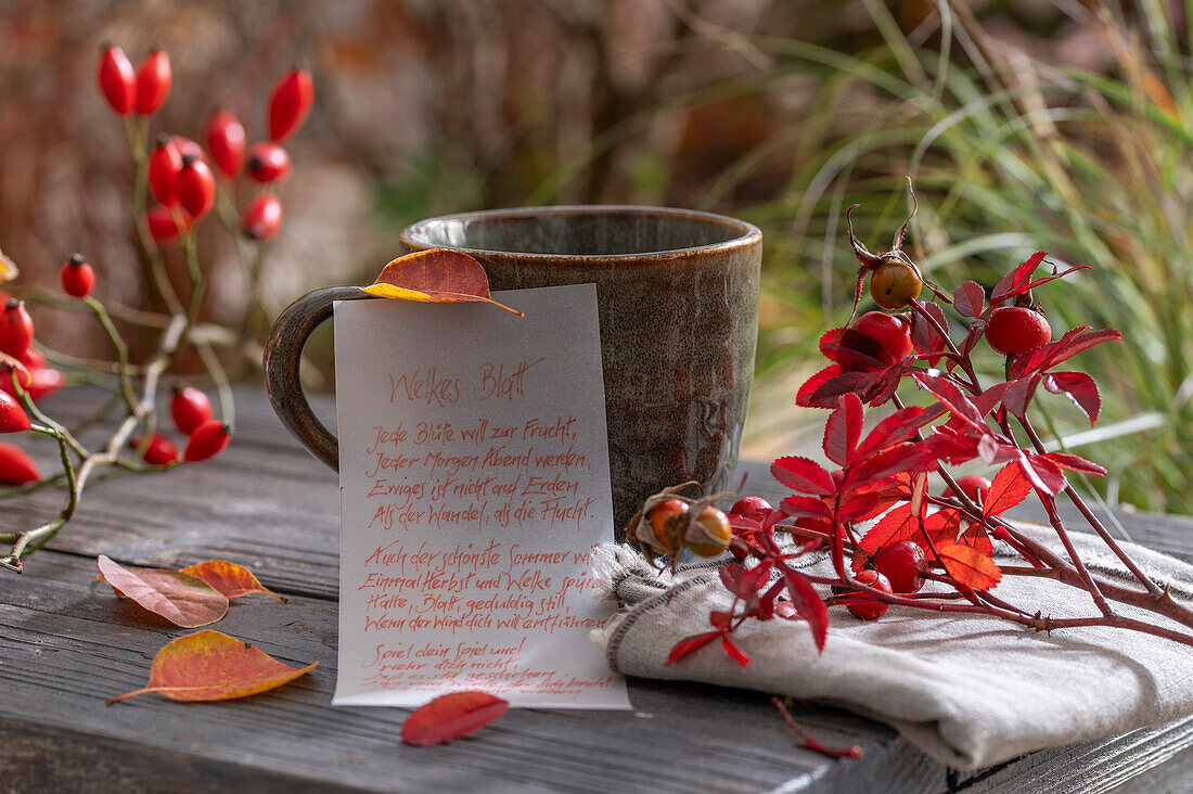 Zettel mit handgeschriebenem Gedicht über Herbstlaub, mit Leinenserviette, Tasse und Hagebutten, Stillleben