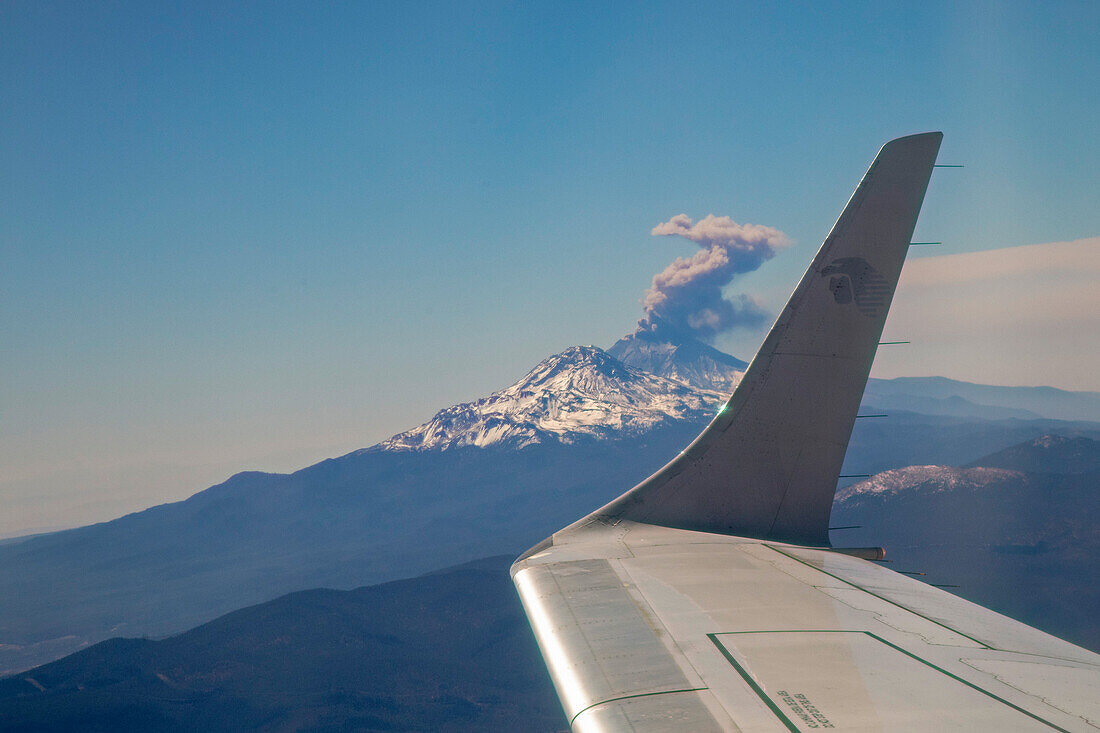 Passenger jet flying past erupting volcano