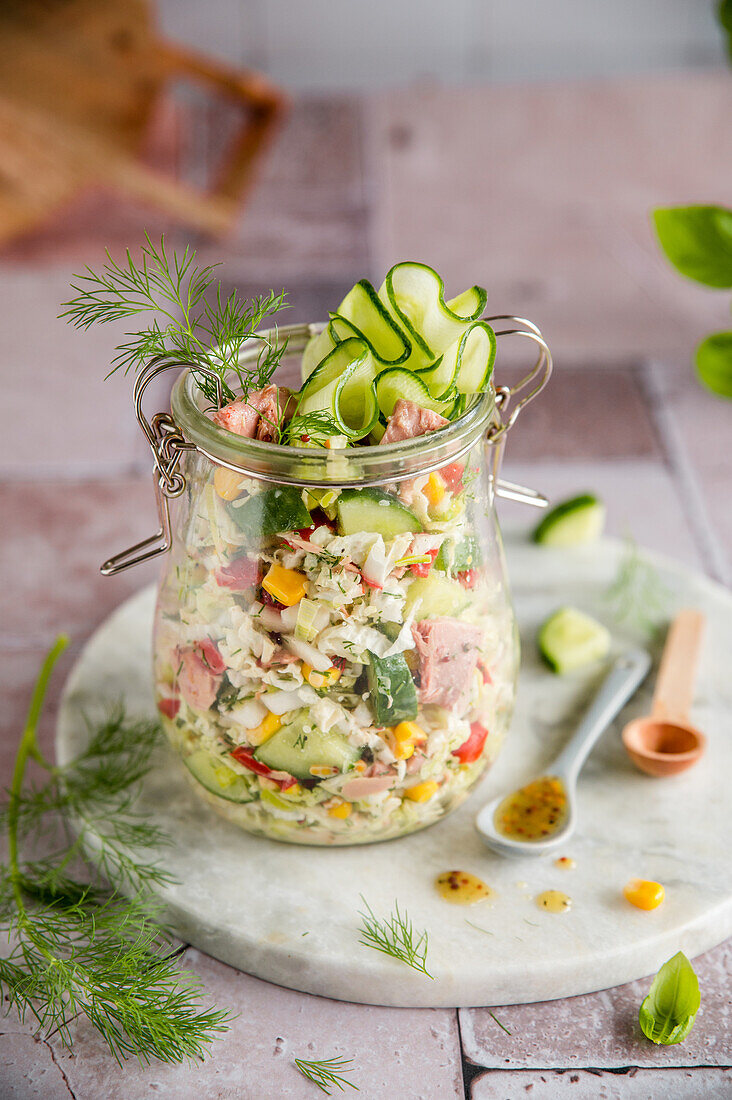 Tuna salad in a jar with fresh herbs and cucumber
