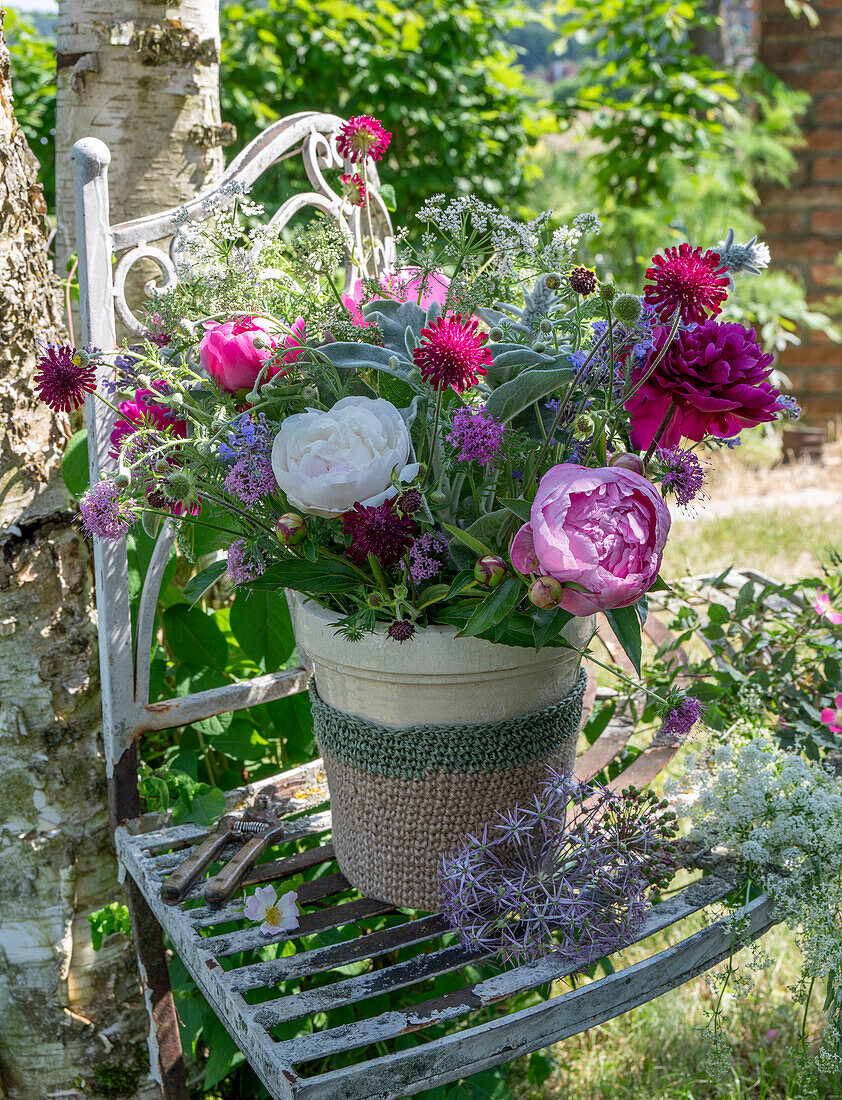 Bunter Strauß aus Pfingstrosen (Paeonia), Scheinwaldmeister, Skabiose, Wollziest, Katzenminze, Giersch und Zierlauch in Vase auf Gartenstuhl