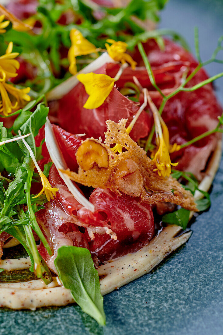 Carpaccio vom geräucherten Rind mit Wildkräutern, Blüten und Parmesanchips