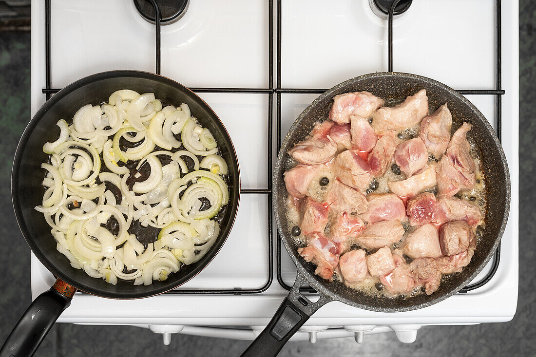 Gebratenes Schweinefleisch und Zwiebelringe in Pfannen