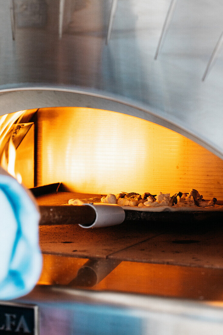 Pizza in den brennenden Pizzaofen schieben