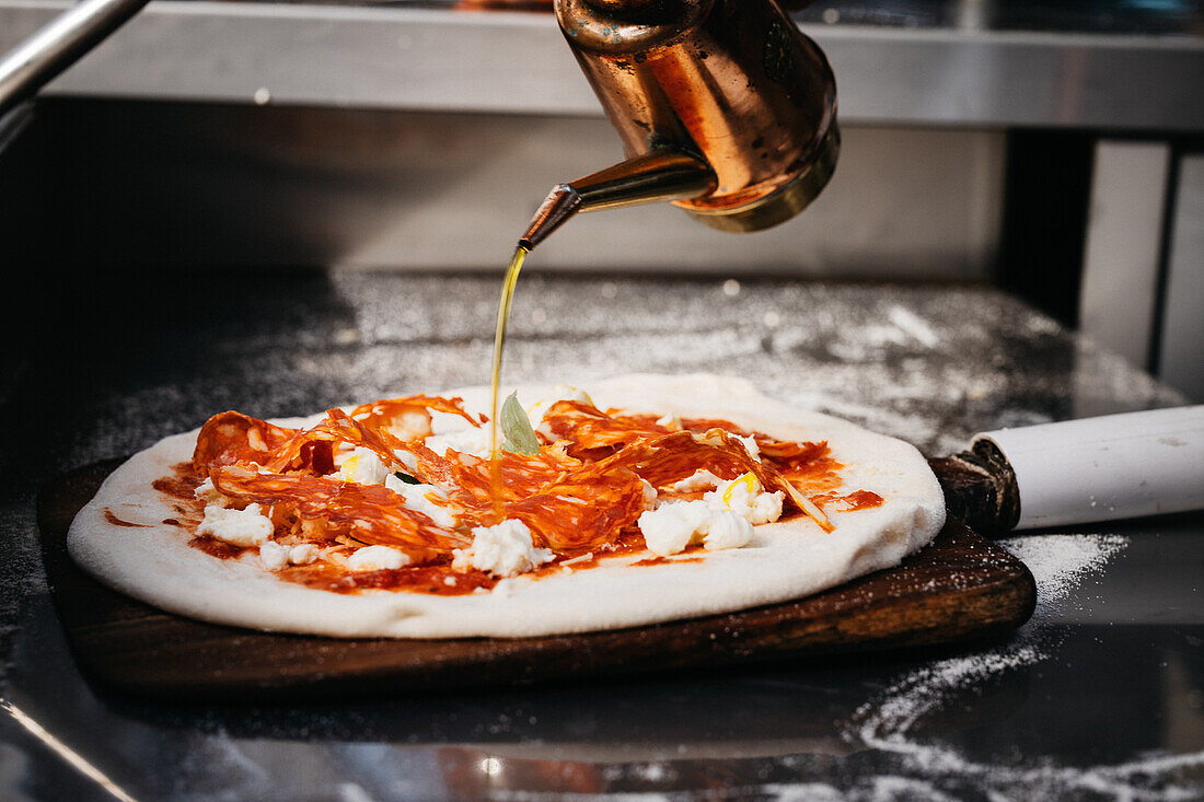 Pizzabäcker begießt Pizza mit Olivenöl
