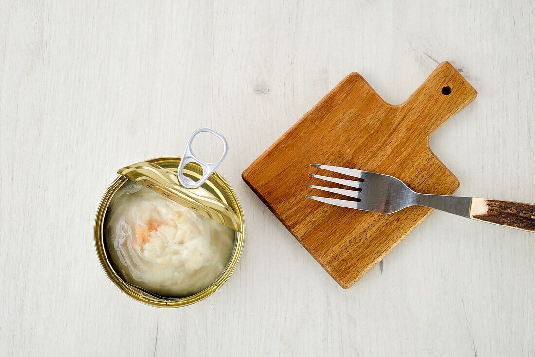 Tinned crab meat next to a chopping board with fork