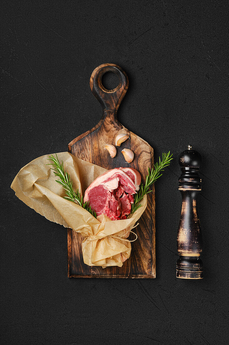 Raw lamb chops in paper on wooden board with rosemary and garlic