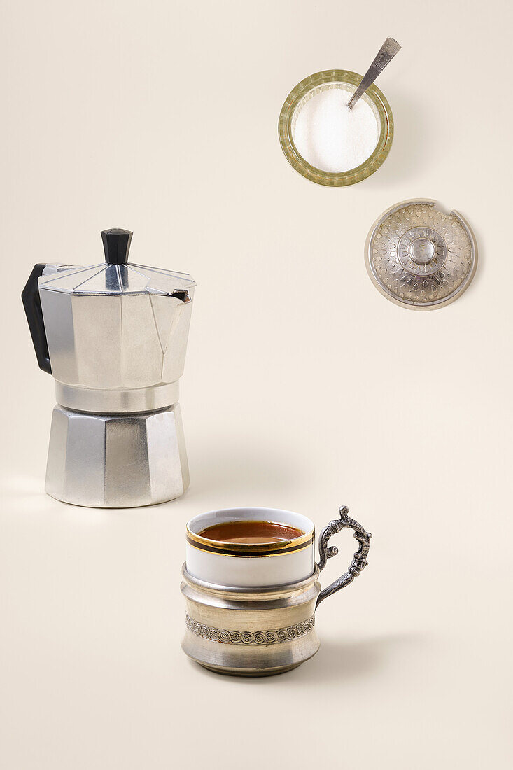 Espresso pot with cup and sugar against a light-coloured background