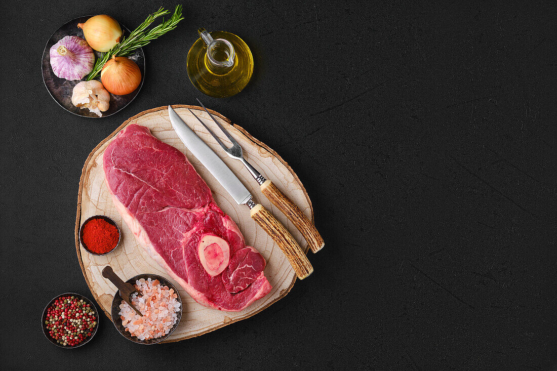 Raw beef steak on a wooden board with spices and oil