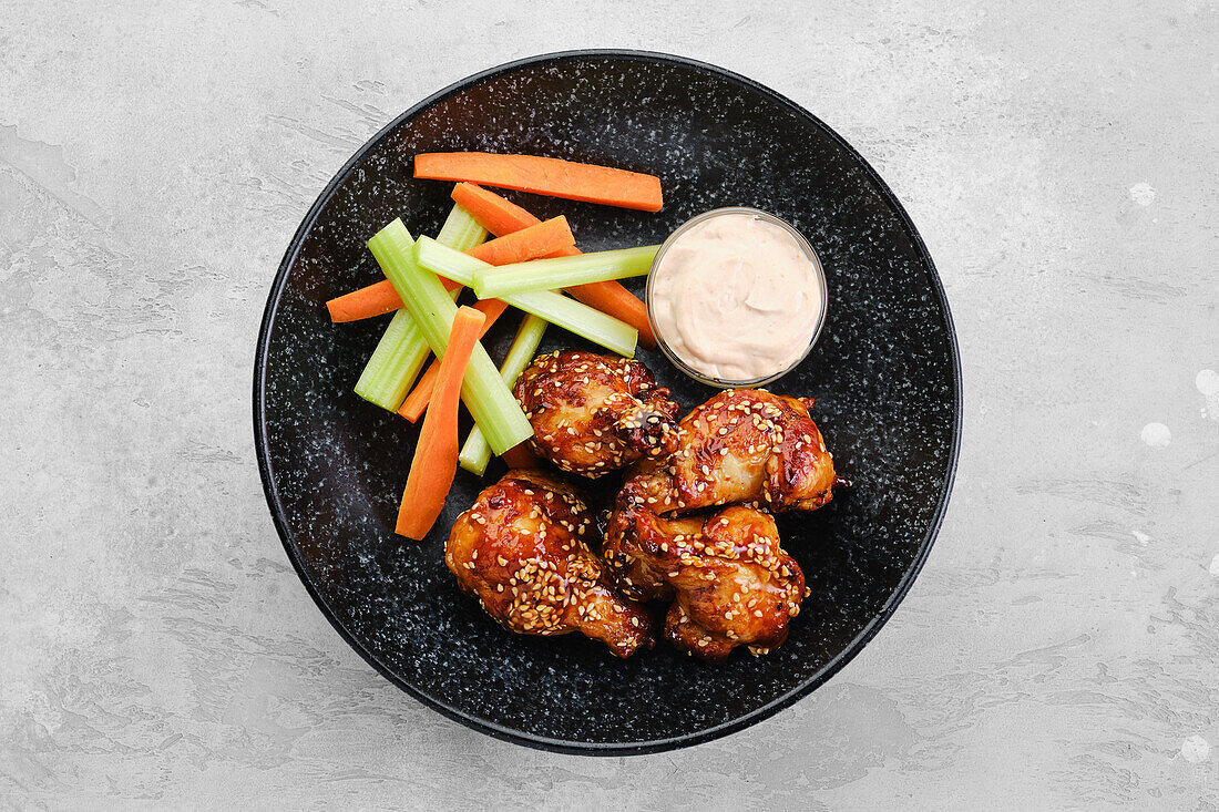 Teriyaki chicken drumsticks with celery and carrot sticks and dip