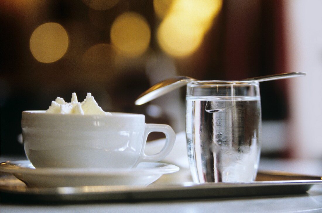 Kaffe Melange mit Sahne & Glas Wasser auf Kaffeehaustisch