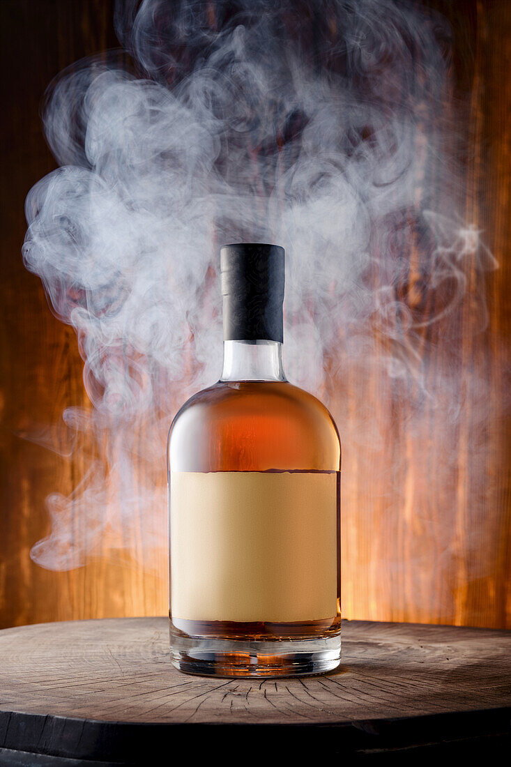 Bottle of smoky malt Scotch whisky with smoke against a wooden background