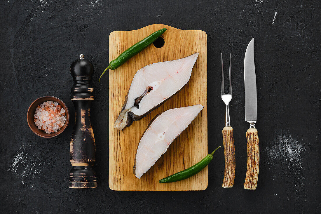 Raw halibut steaks on a wooden board with chilli and sea salt