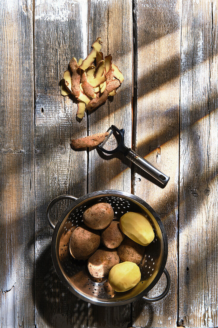 Potatoes in metal sieve, partly peeled