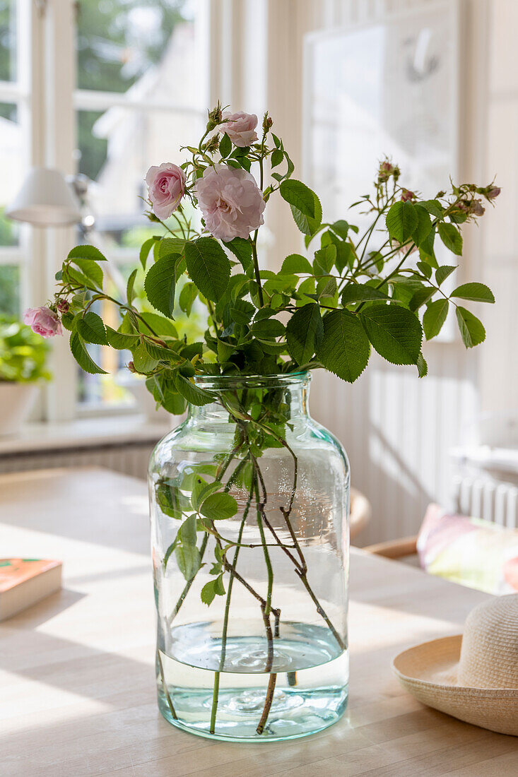 Blumen in Glasvase auf hellem Holztisch vor Fenster