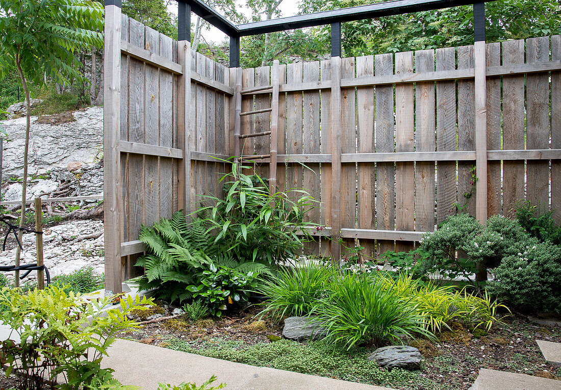 Holzzaun mit üppigen Gartenpflanzen in einer Ecke des Gartens