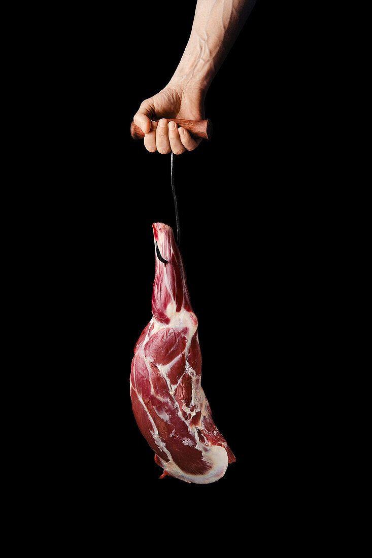 Hand holding raw leg of lamb on a hook