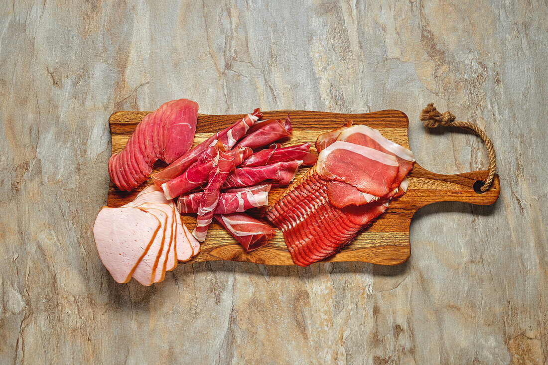 Various types of sausage and ham on a wooden board