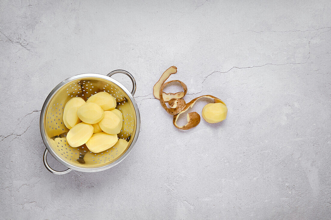 Peeled potatoes in a sieve on a grey base