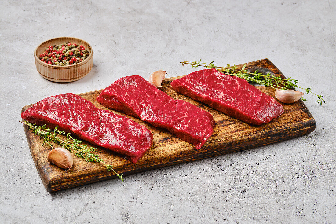 Raw beef steaks on wooden board with spices