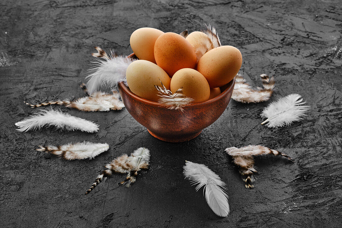 Brown eggs in a clay bowl with chicken feathers