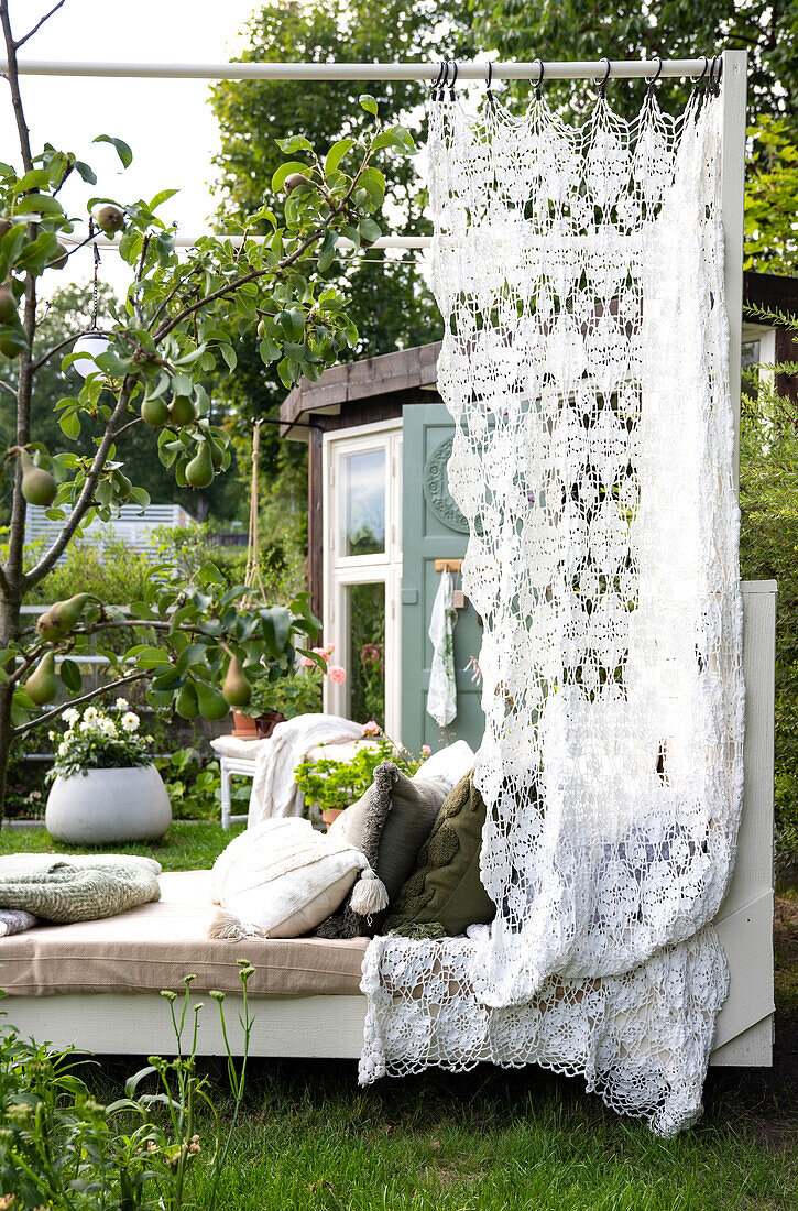 Sonnenbett mit gehäkeltem Vorhang und Kissen im Garten