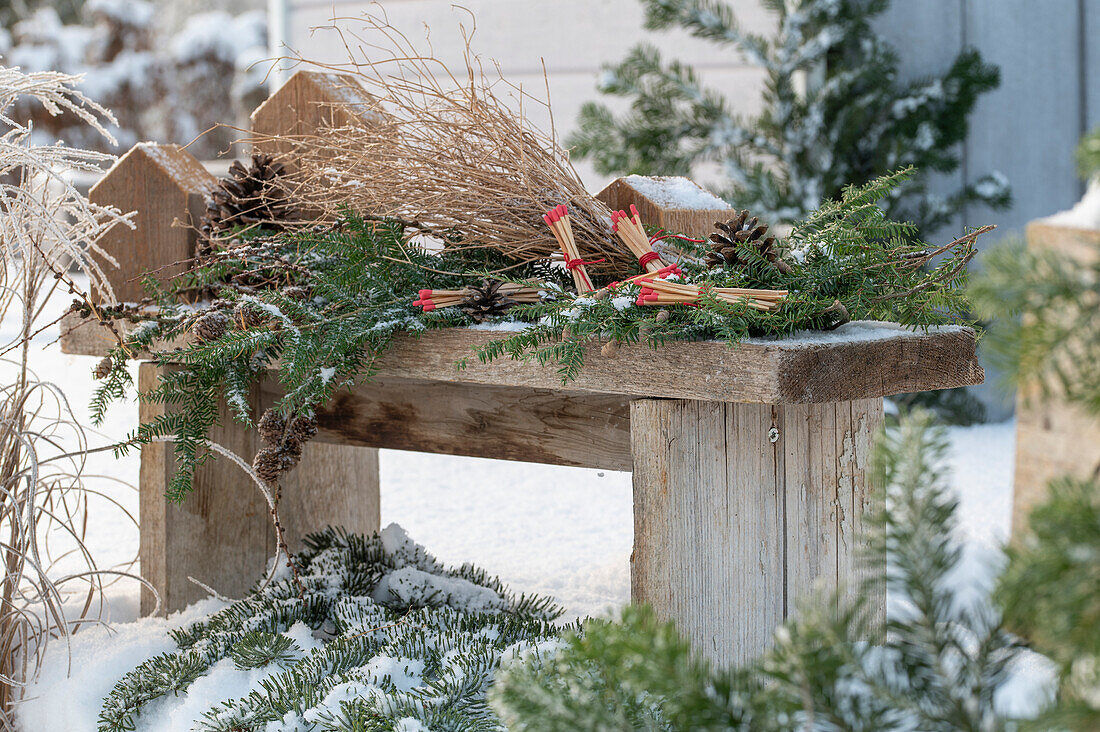 Zündhölzer auf Tannenzweigen und Zapfen im verschneiten Garten