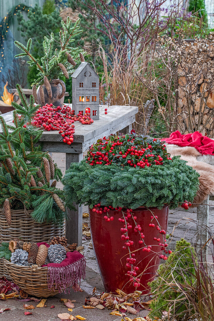 Weihnachtsbasteln auf der Terrasse, Adventskranz aus Tannenzweigen, roten Beeren des Zierapfels, Fichtenzweige und Zapfen im Korb, Häuschen mit Kerze am Tisch