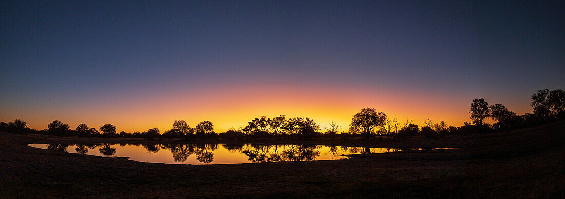 Farbenfroher Sonnenuntergang am Wasserloch. Camelthorn Lodge. Hwange-Nationalpark. Simbabwe.