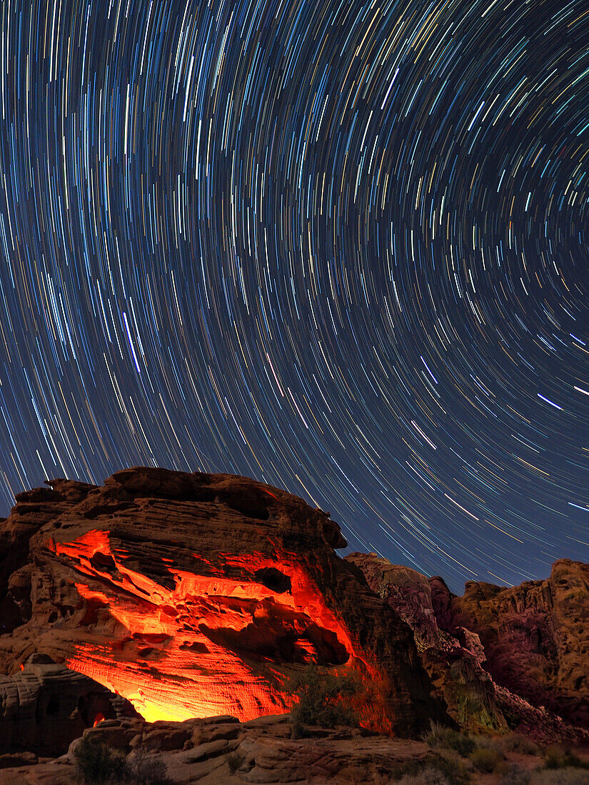 Usa, Nevada. Valley of Fire State Park, star trails and campfire glowing in sandstone rocks