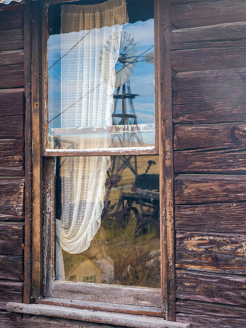 USA, Bundesstaat Washington, Molson, Okanogan County. Spiegelung der Windmühle und des Traktors im Fenster eines alten Gebäudes in der historischen Geisterstadt.