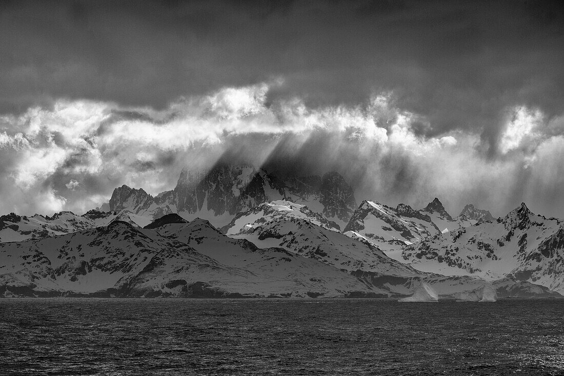 Black and white of South Georgia Island. Opening in clouds and Virga reveal the mountainous and glaciated landscape.