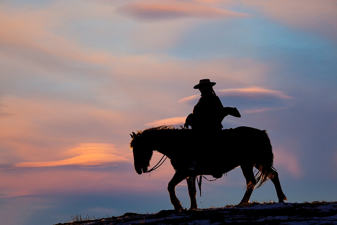USA, Shell, Wyoming. Cowgirl der Hideout Ranch auf dem Pferderücken bei Sonnenuntergang. (PR,MR)