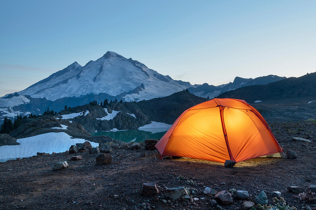 Red Big Agnes backpacking tent illuminated at twilight at backcountry camp on Ptarmigan Ridge. Mount Baker Wilderness. North Cascades, Washington State